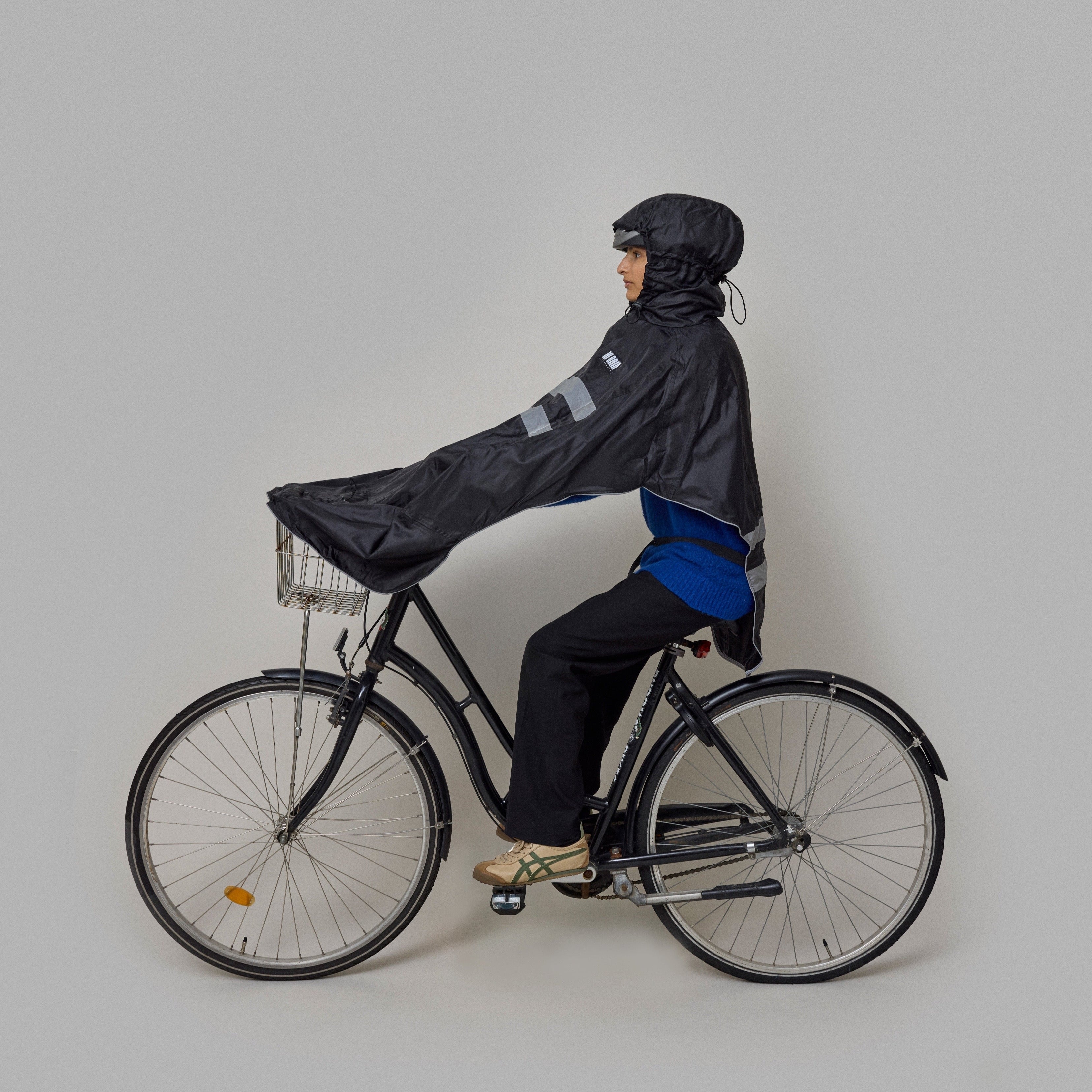 Person riding a bicycle wearing a black NoRain Bicycle Poncho on a plain background