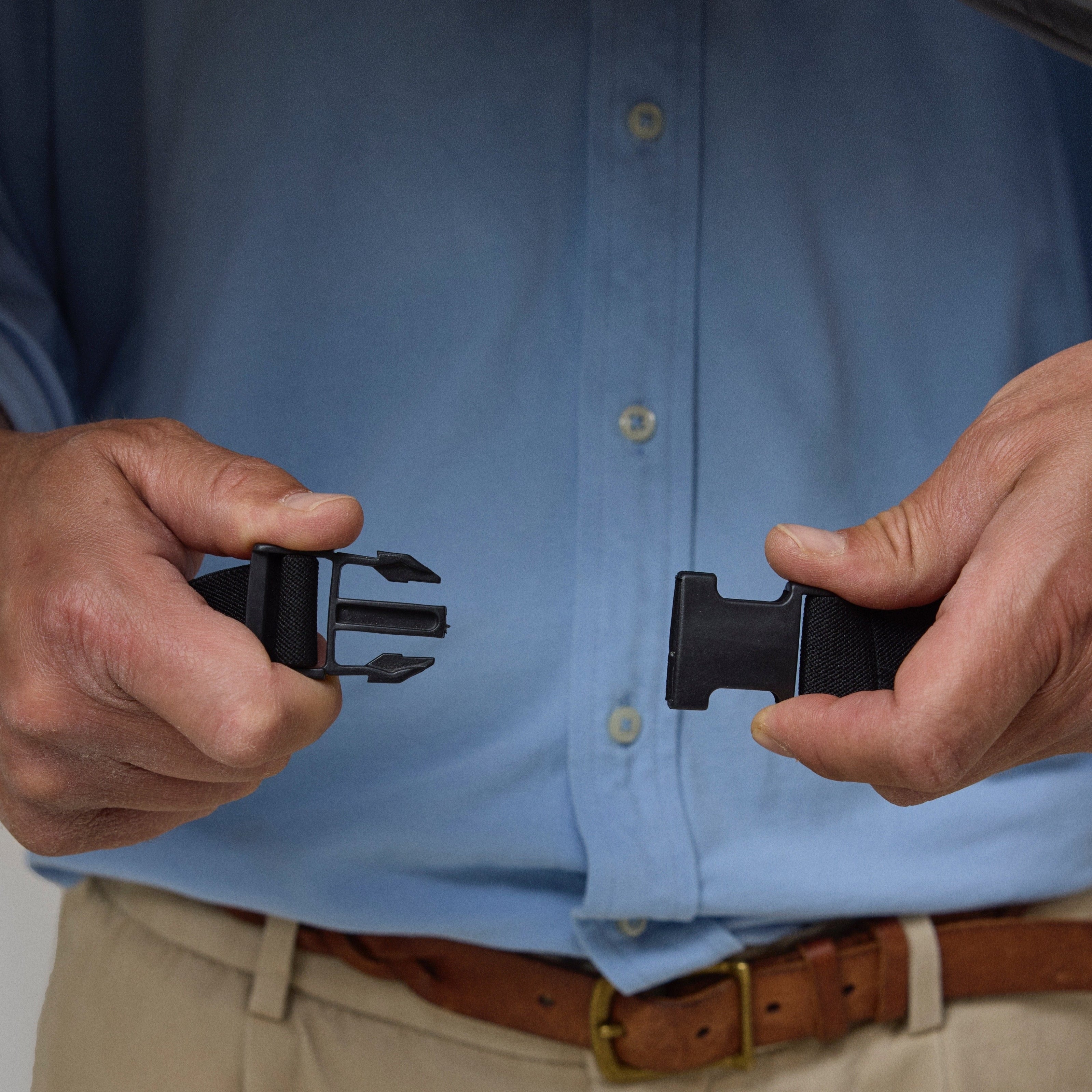 Person holding a black belt with a clip on the NoRain Bicycle poncho, wearing a blue shirt and beige pants.