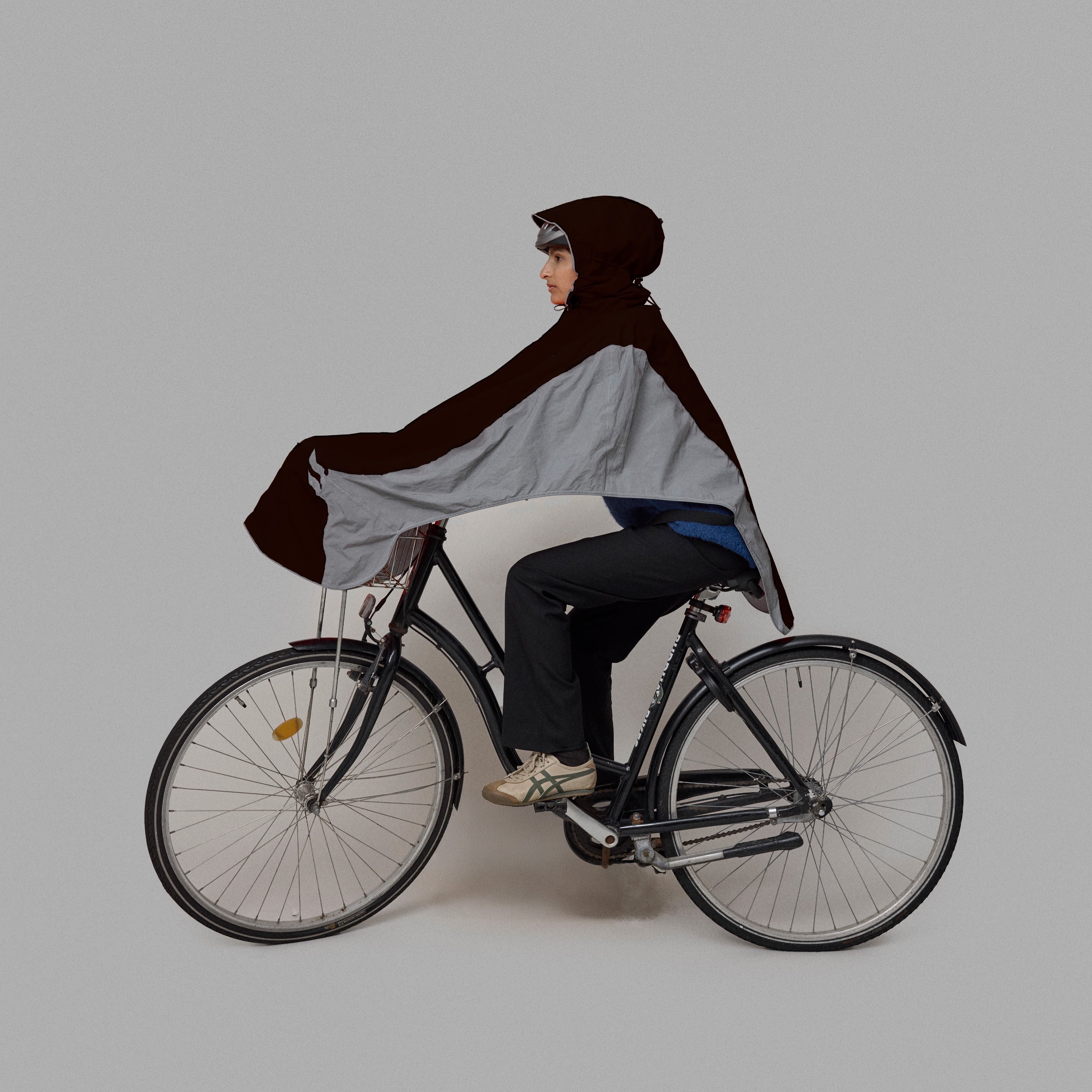 Person riding a bicycle wearing a dark and chrome NoRain bicycle poncho on a plain background