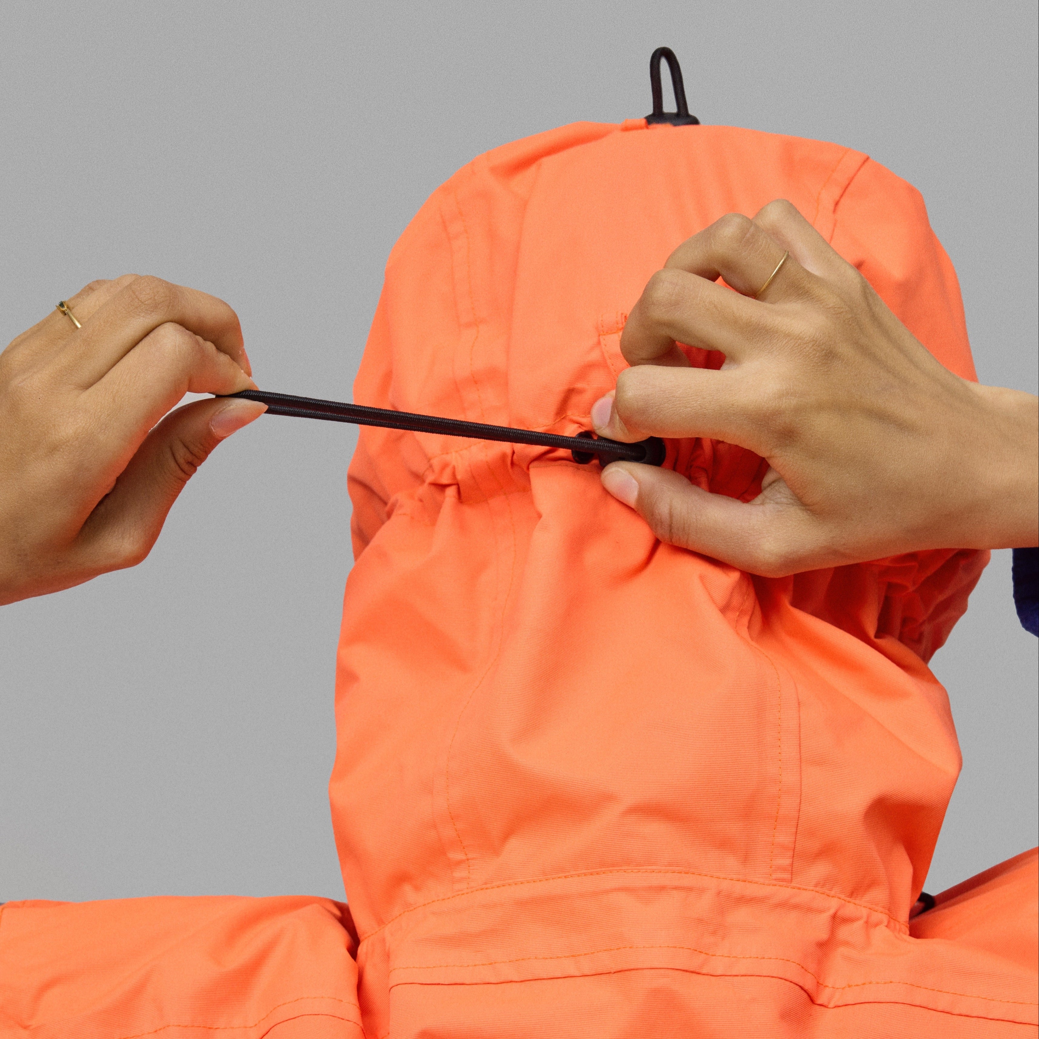 Orange NoRain bicycle poncho hoodie being adjusted on a gray background