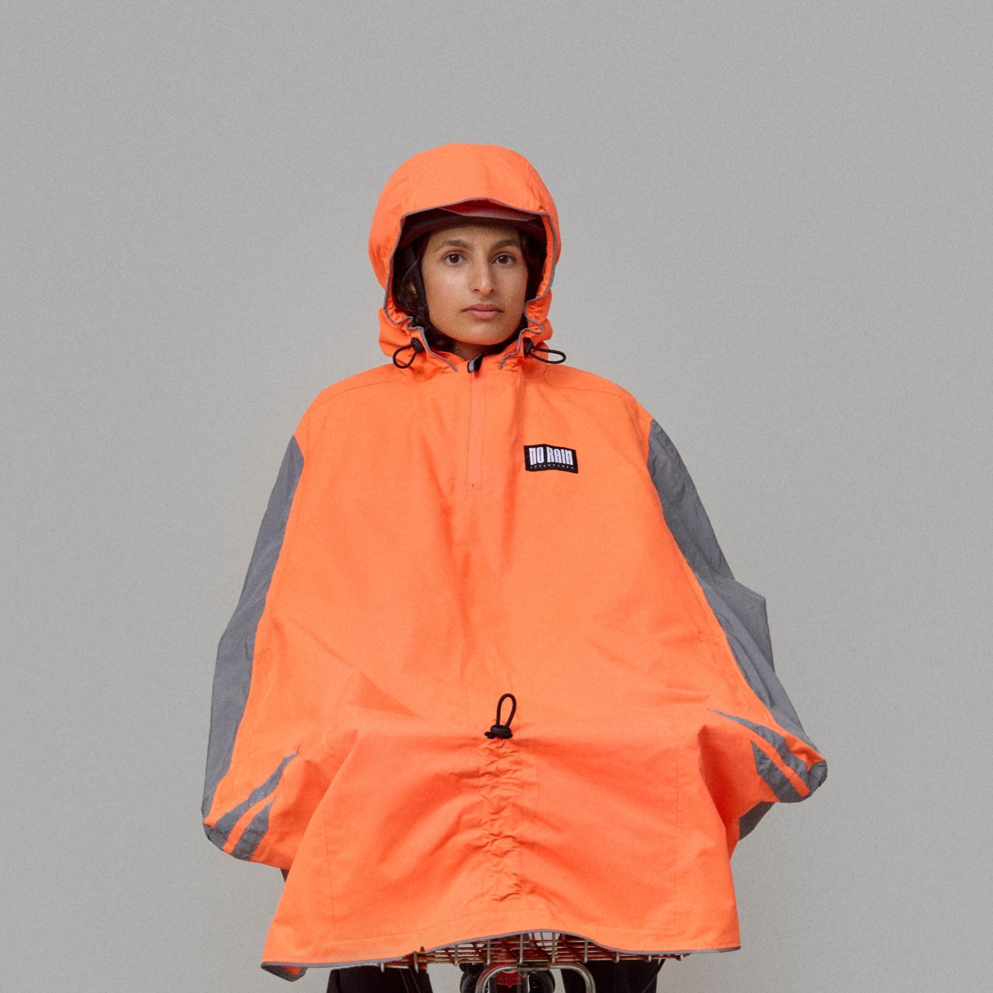 Person riding a bicycle wearing an orange NoRain bicycle poncho on a gray background