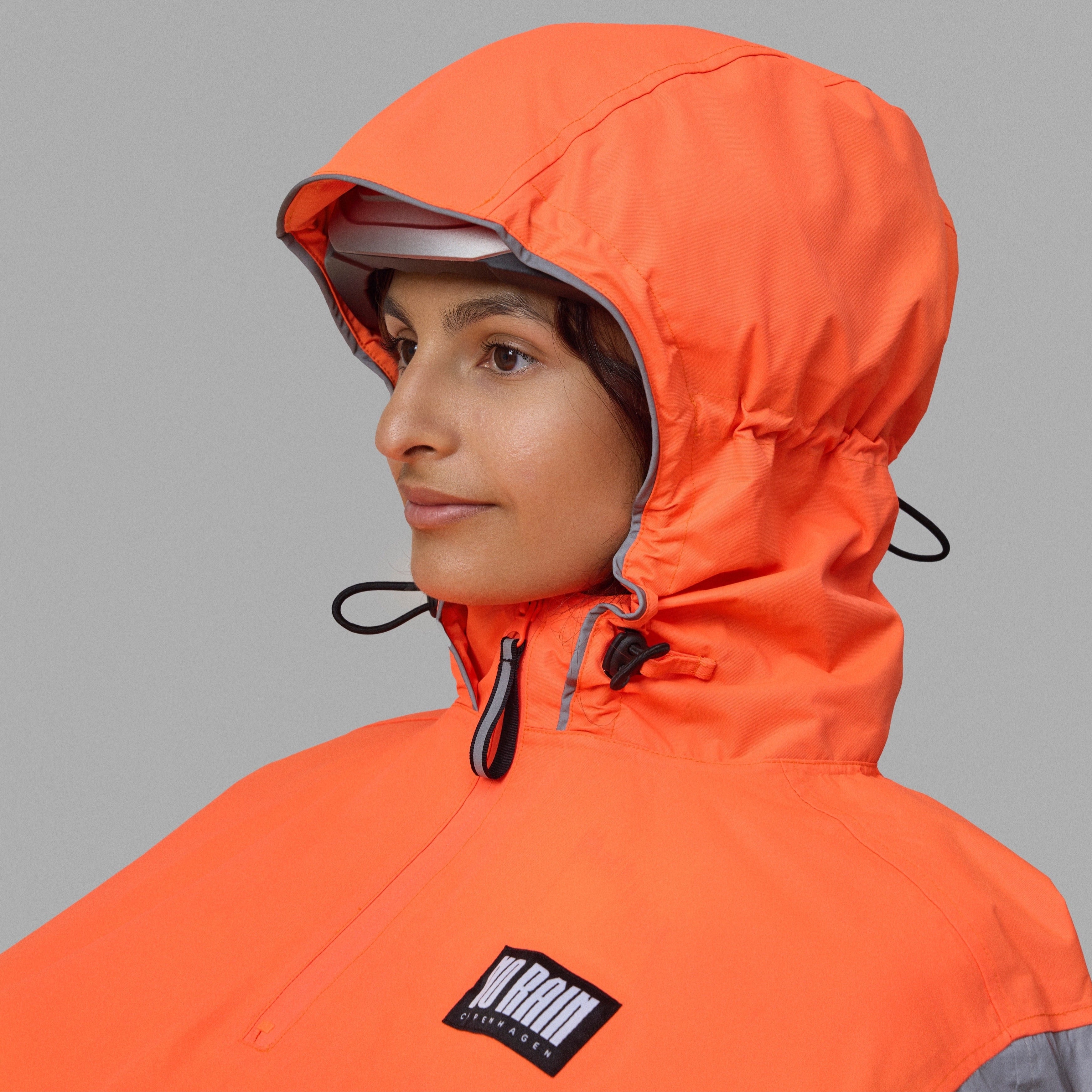 Person wearing an orange NoRain bicycle poncho with a brand logo on a gray background
