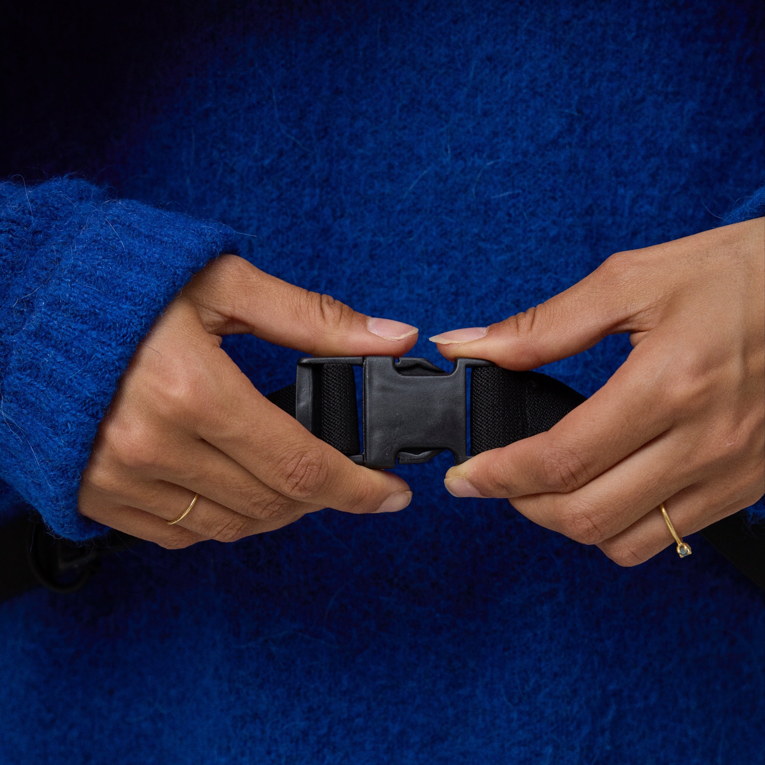 Person wearing a blue sweater with hands adjusting a black belt strap of the NoRain bicycle poncho.