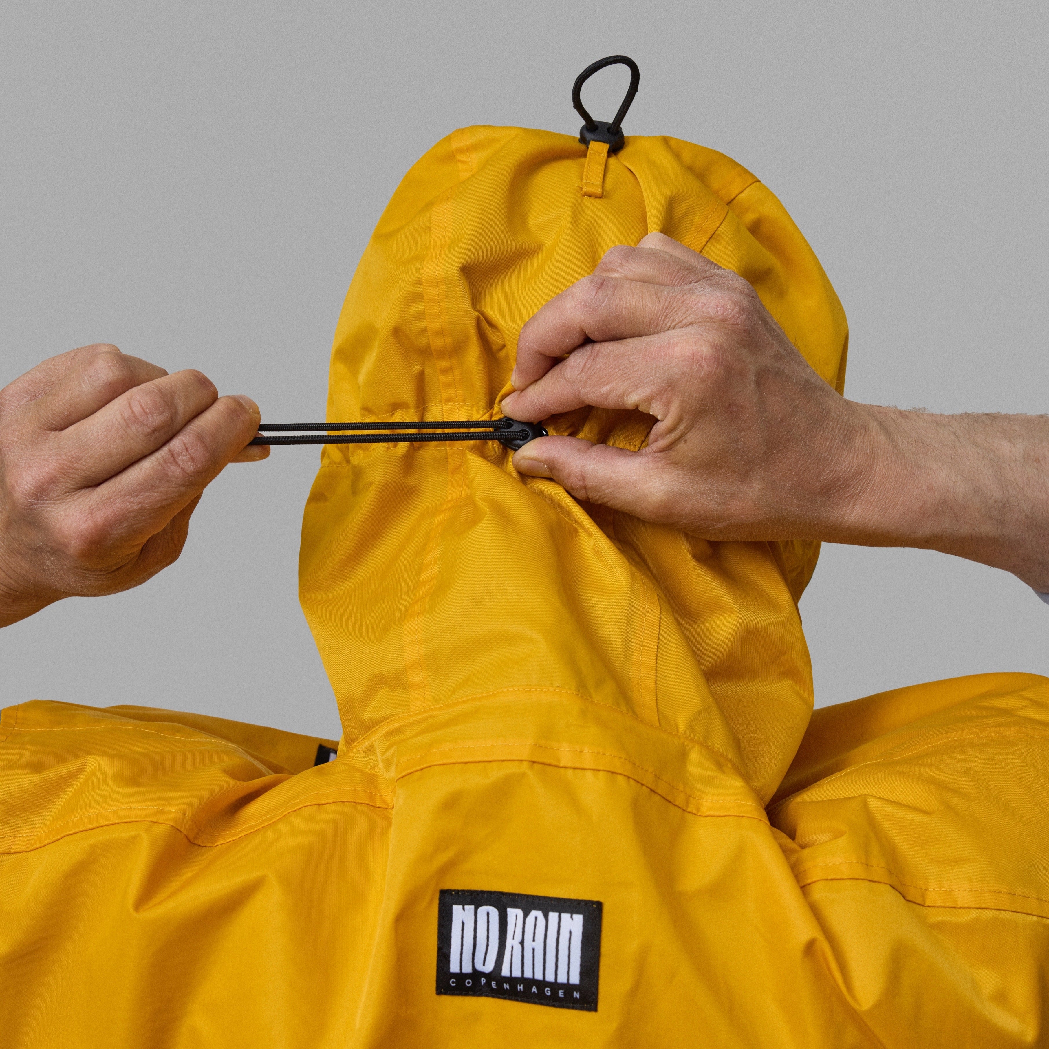 Person adjusting a yellow NoRain bicycle poncho with 'NoRain' logo on a gray background