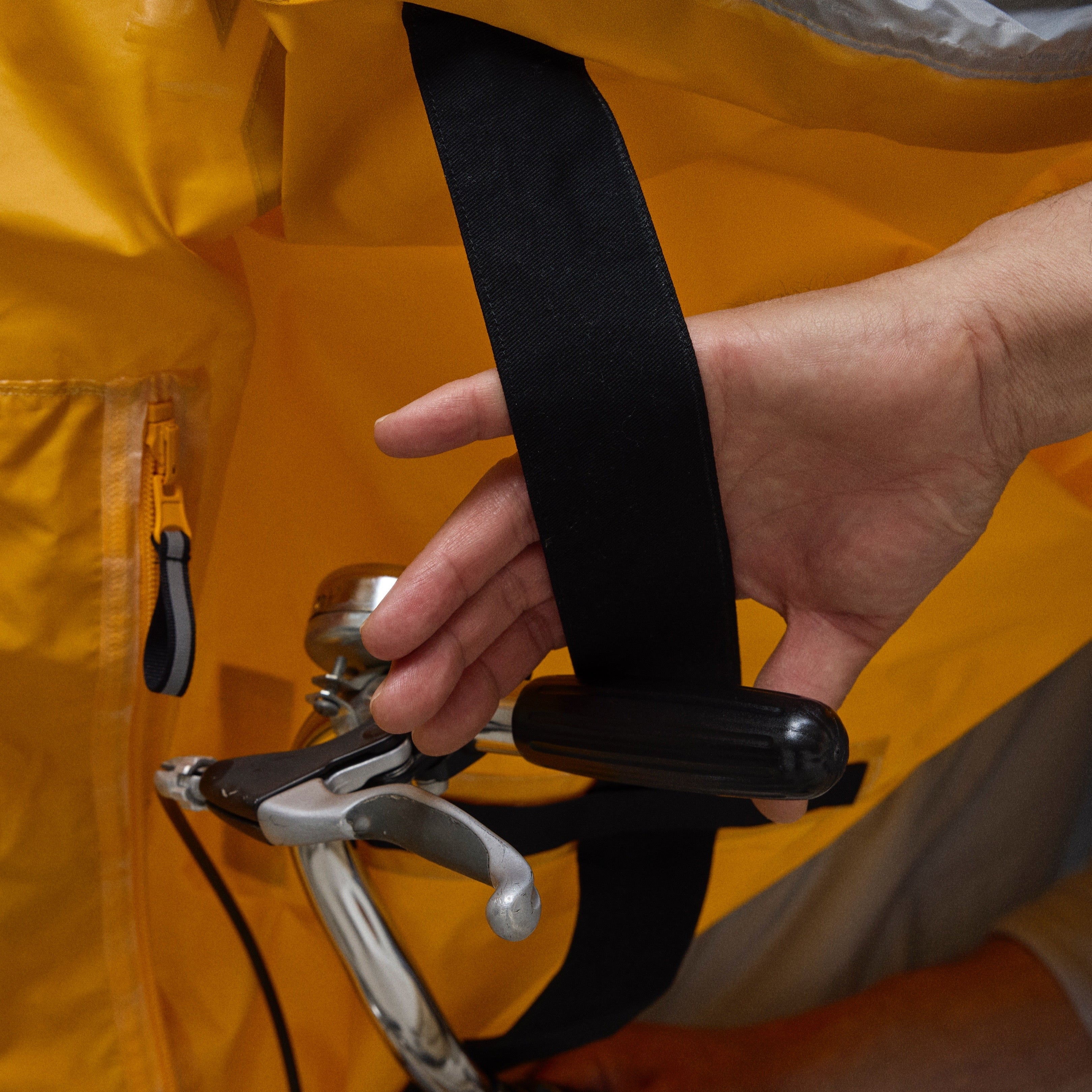 Person adjusting a black strap on a yellow NoRain bicycle poncho with a gray background