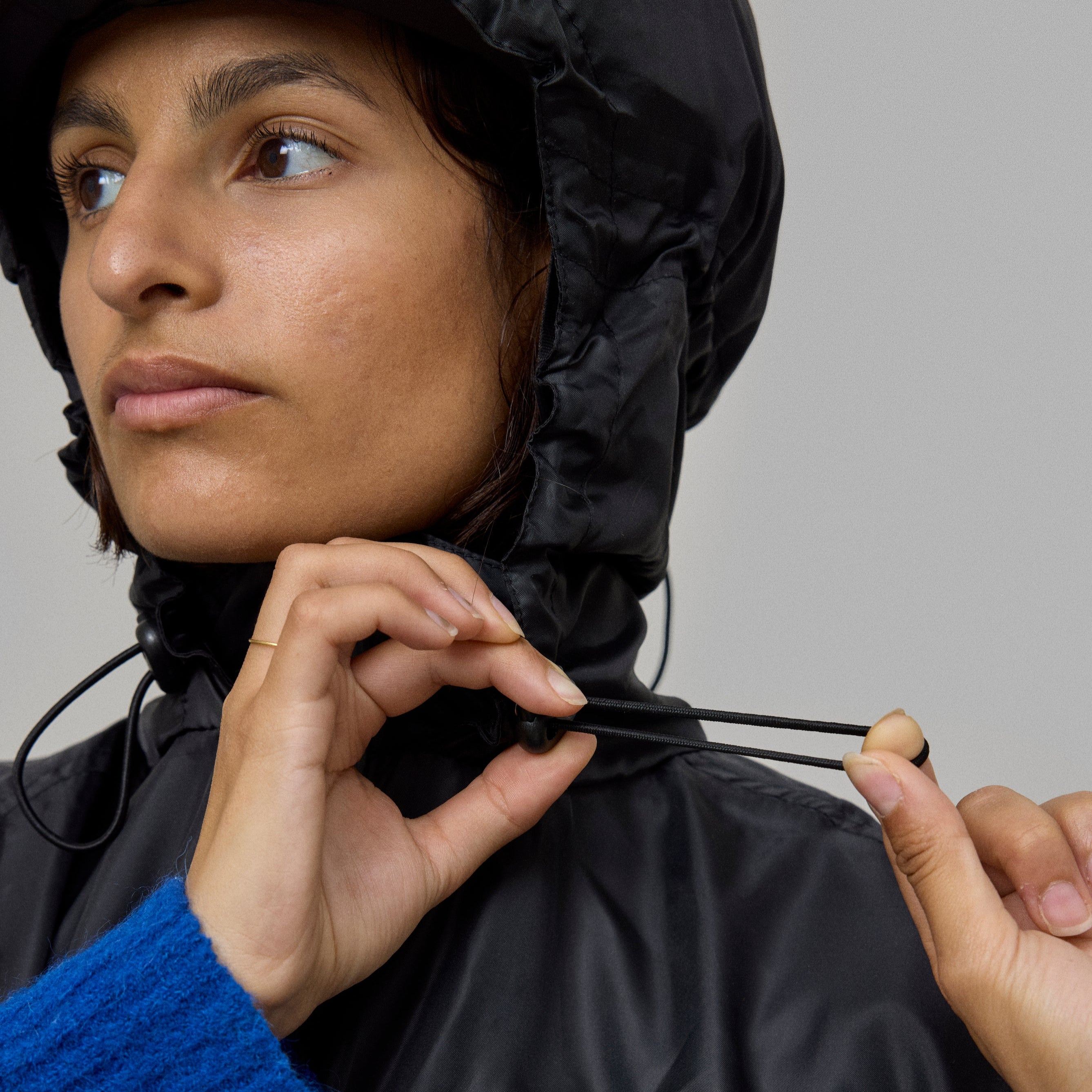 Person wearing a black bicycle poncho with 'NO RAIN' logo, adjusting hood against a neutral background