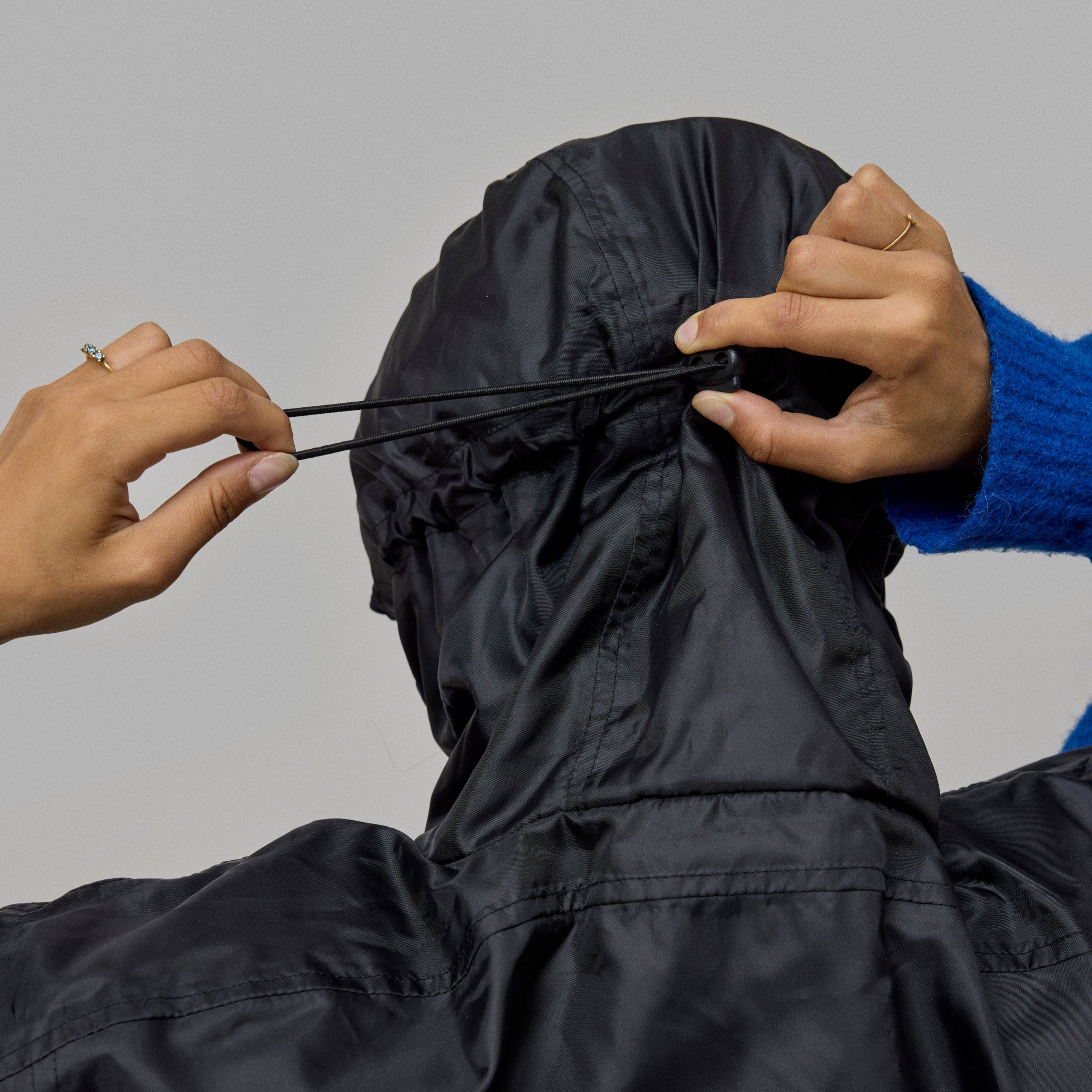 Person adjusting the hood of a black NoRain Poncho with 'No Rain' logo on a gray background