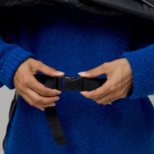 Person wearing a blue sweater and black NoRain bike poncho, adjusting a black belt.