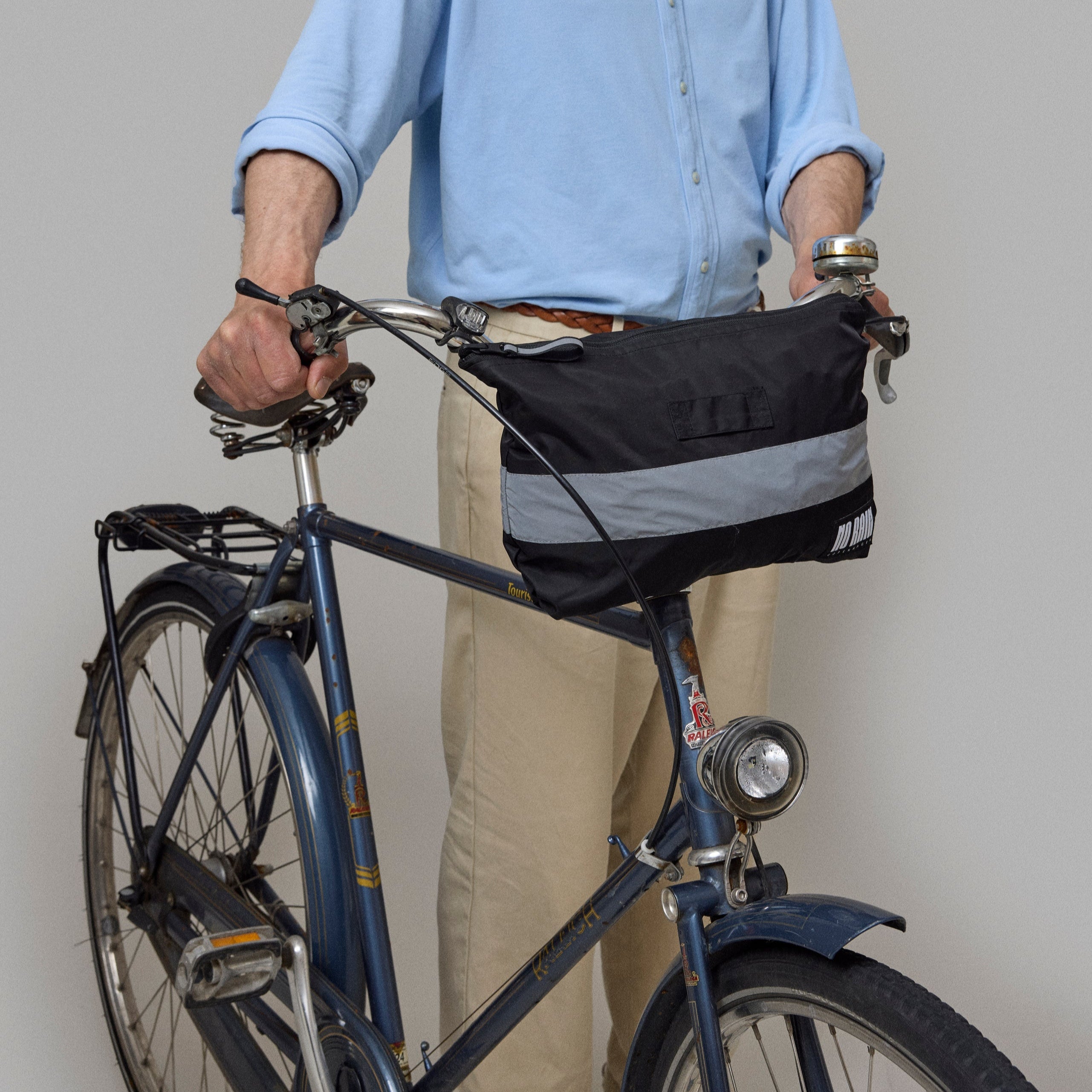 Man standing next to a bicycle with a norain poncho folded into a bag on a plain background