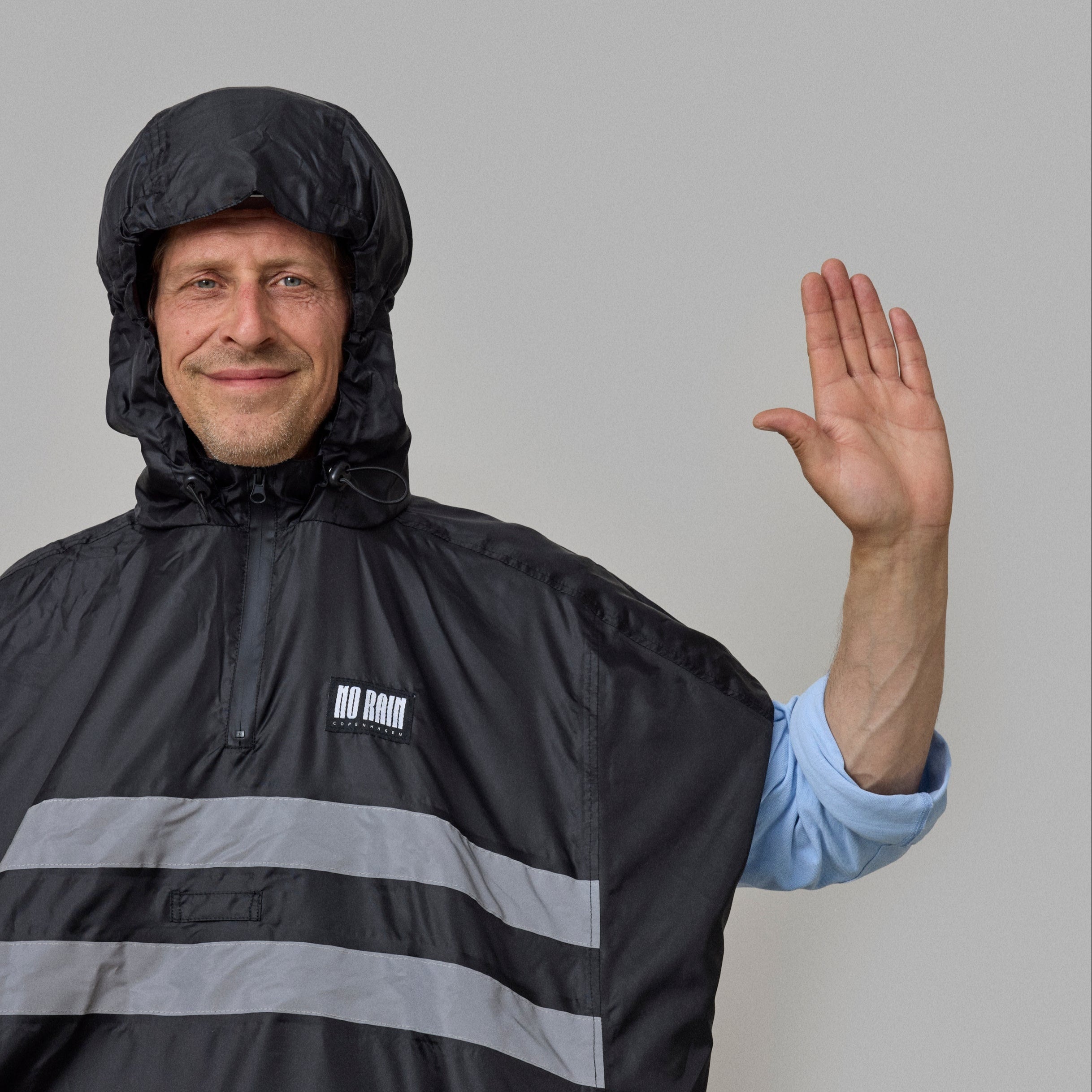 Person wearing a black NoRain Copenhagen bicycle rain poncho with reflective stripes on a gray background