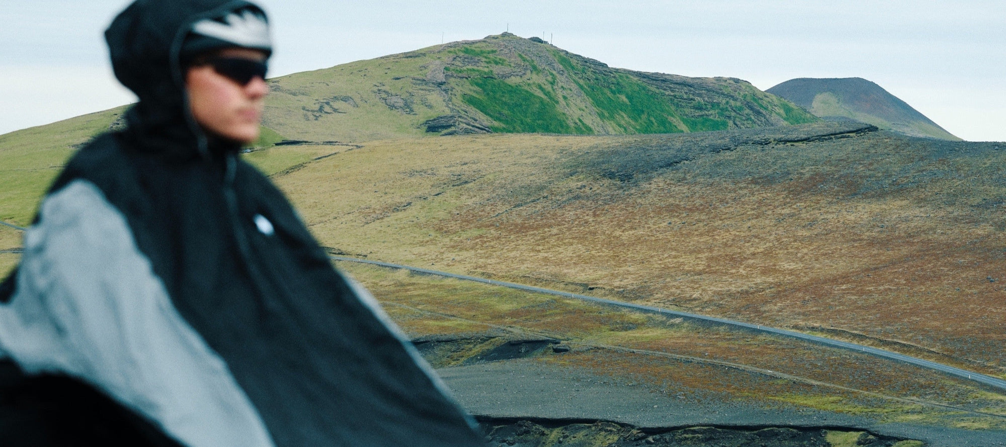 Person cycling on a road with a norain poncho with a scenic mountain landscape in the background
