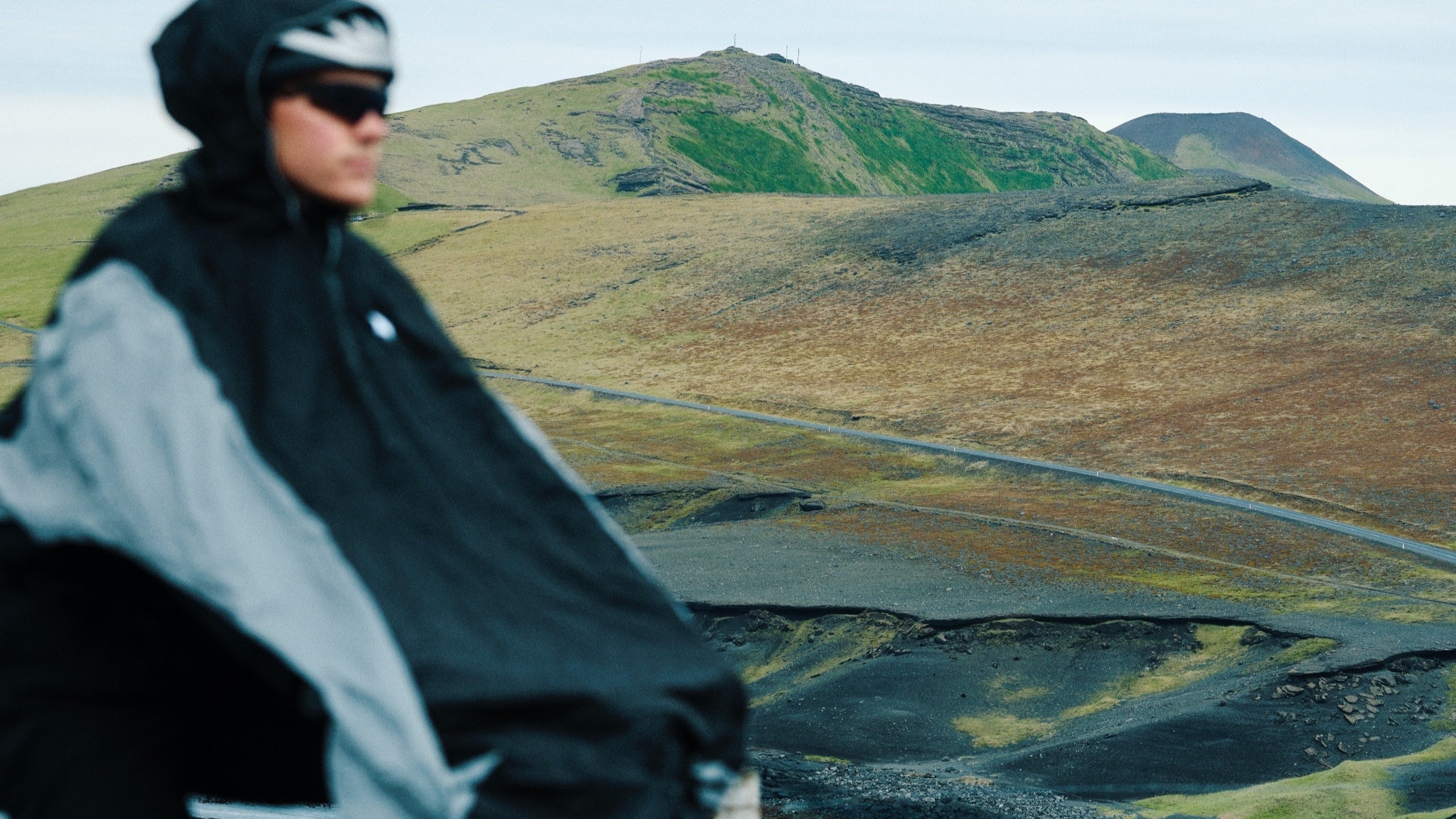 Person cycling on a road with a norain poncho with a scenic mountain landscape in the background