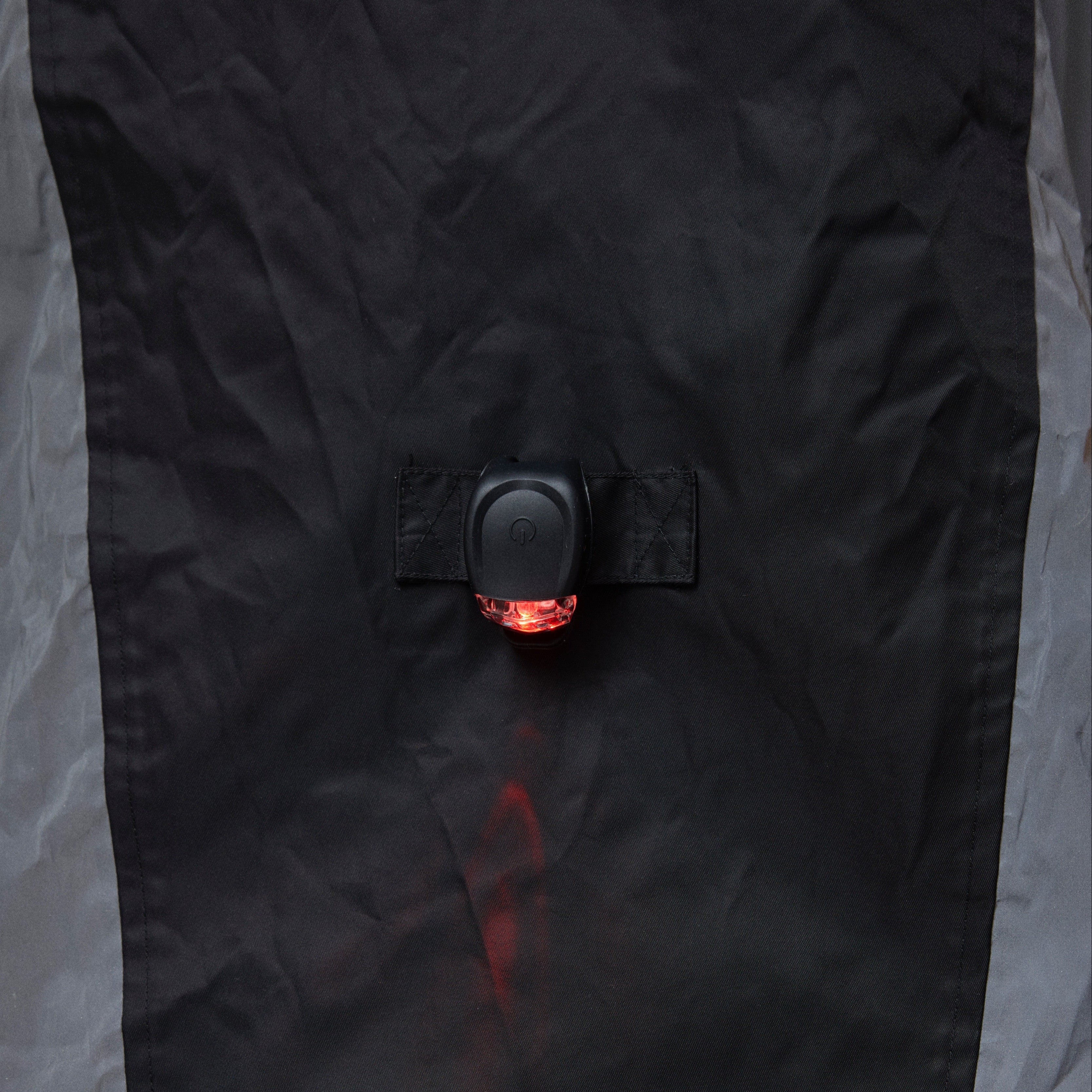 Close-up of a black NoRain Bicycle poncho with a button and red light on a gray background