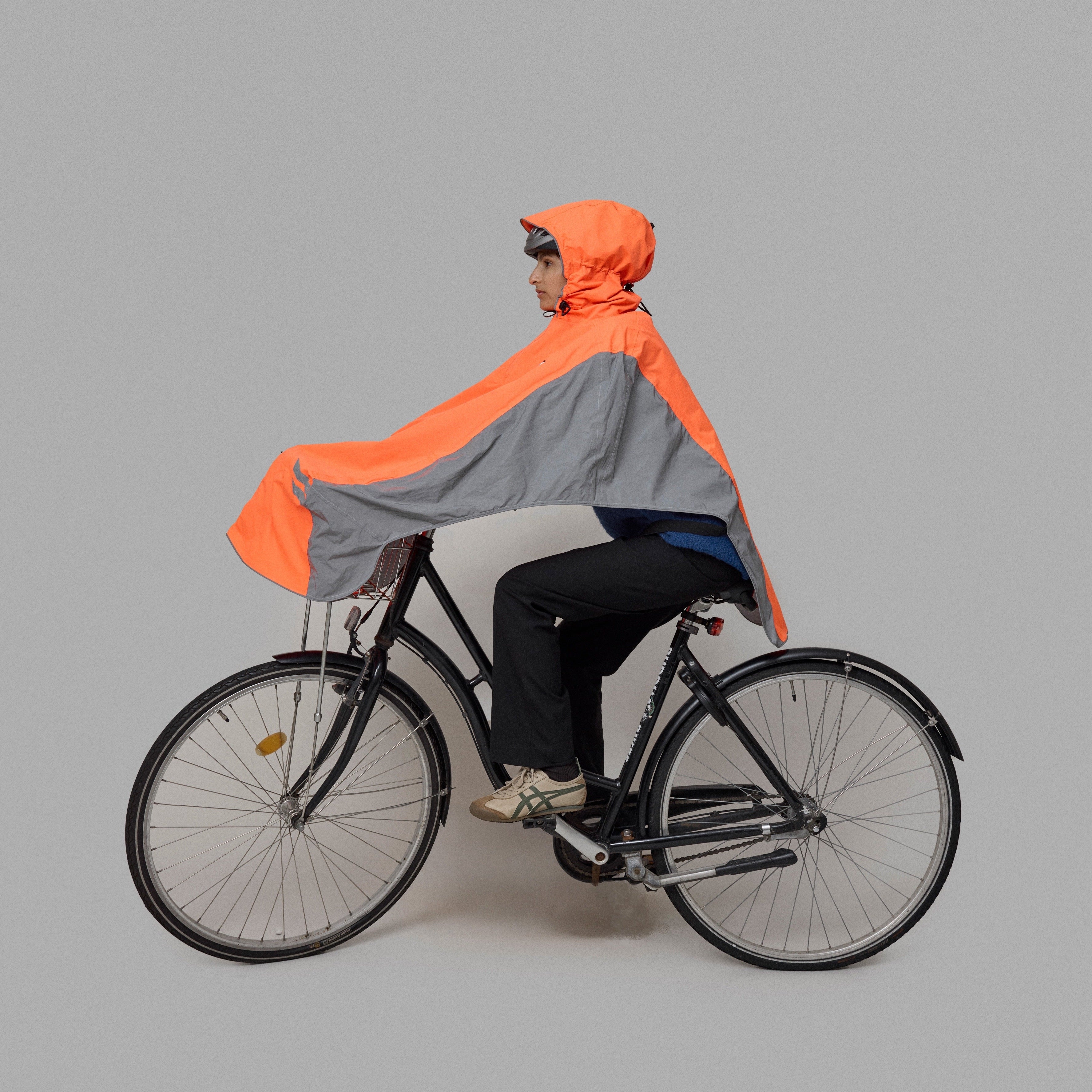 Person riding a bicycle wearing an orange and gray NoRain bicycle poncho  on a plain background