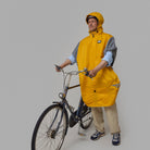 Person wearing a yellow NoRain bicycle poncho  standing next to a bicycle on a plain background