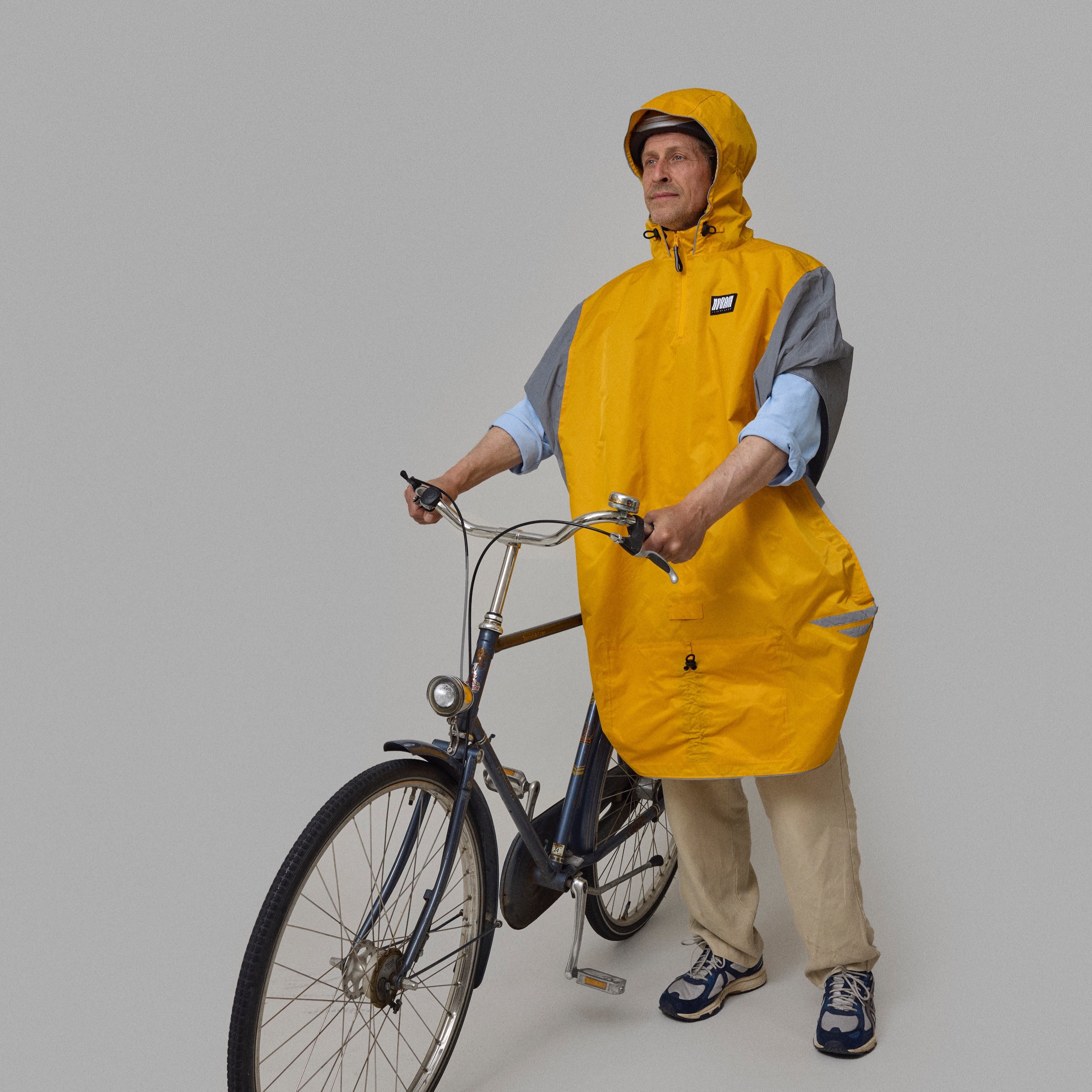Person wearing a yellow NoRain bicycle poncho  standing next to a bicycle on a plain background