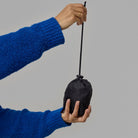 Person holding a black drawstring bag, which is a foldable NoRain backpack, against a gray background.