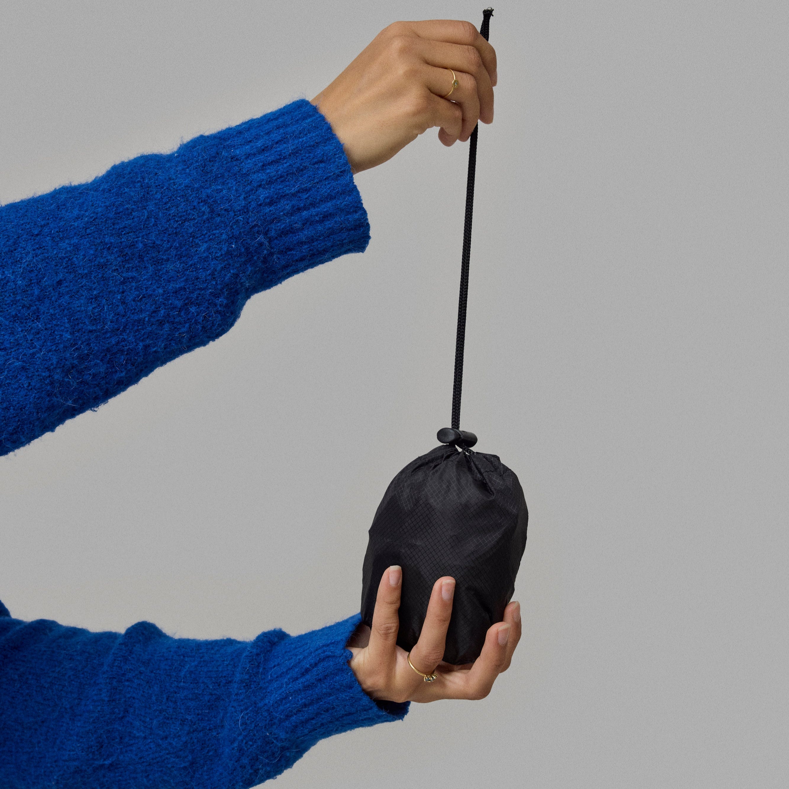 Person holding a black drawstring bag, which is a foldable NoRain backpack, against a gray background.