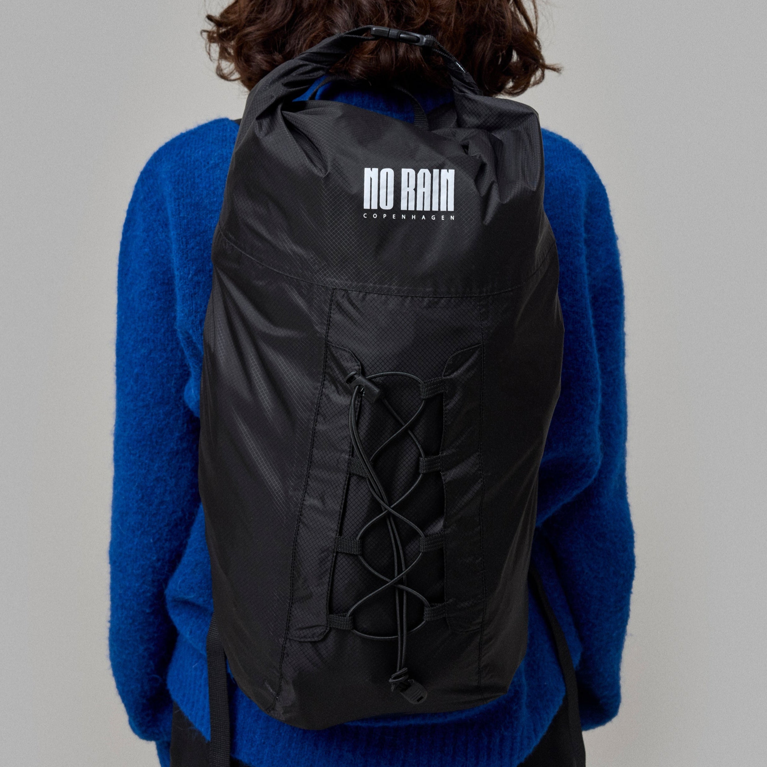 Person wearing a black waterproof Norain  backpack with 'No Rain' logo on a gray background