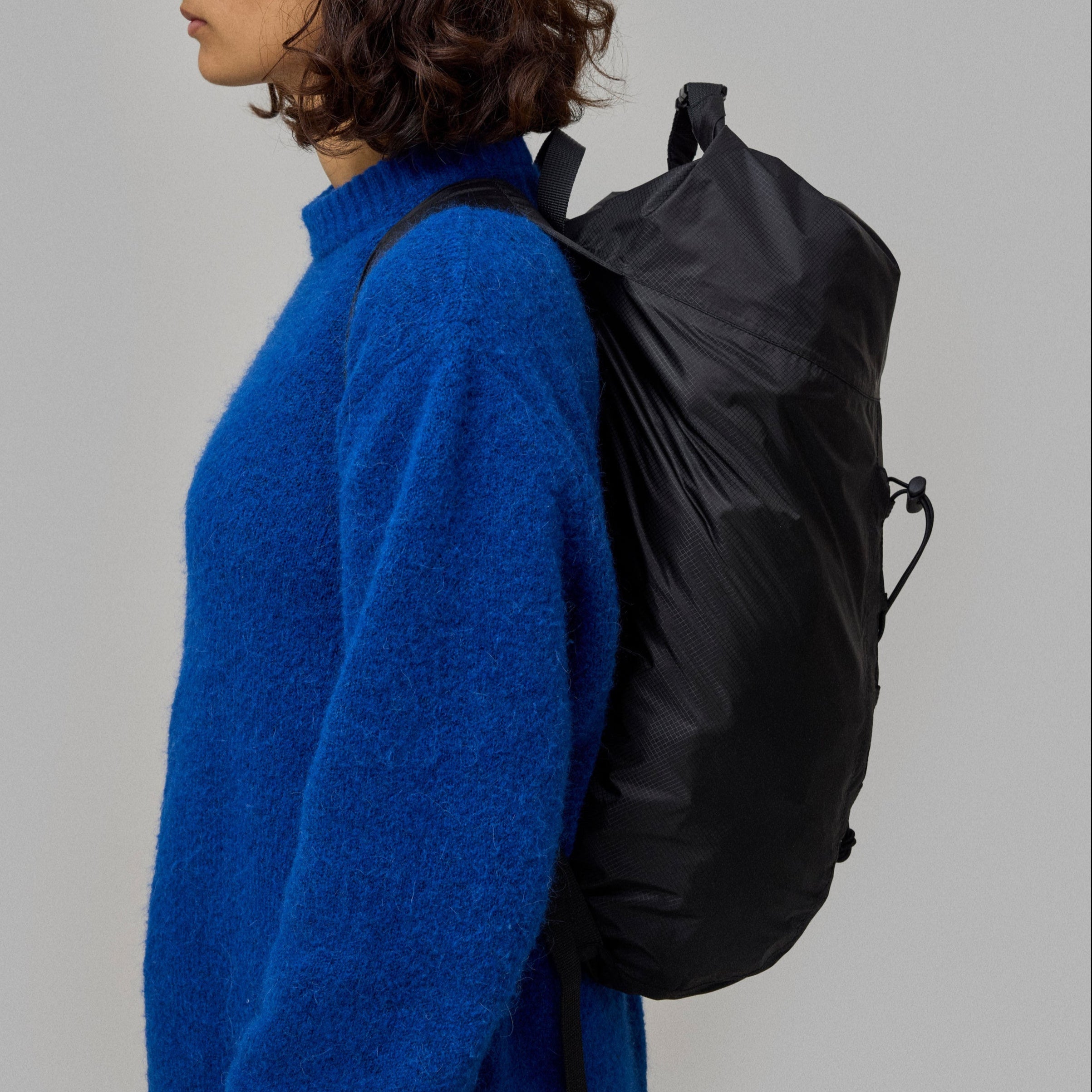 Person wearing a blue sweater with a waterproof norain black backpack on a gray background