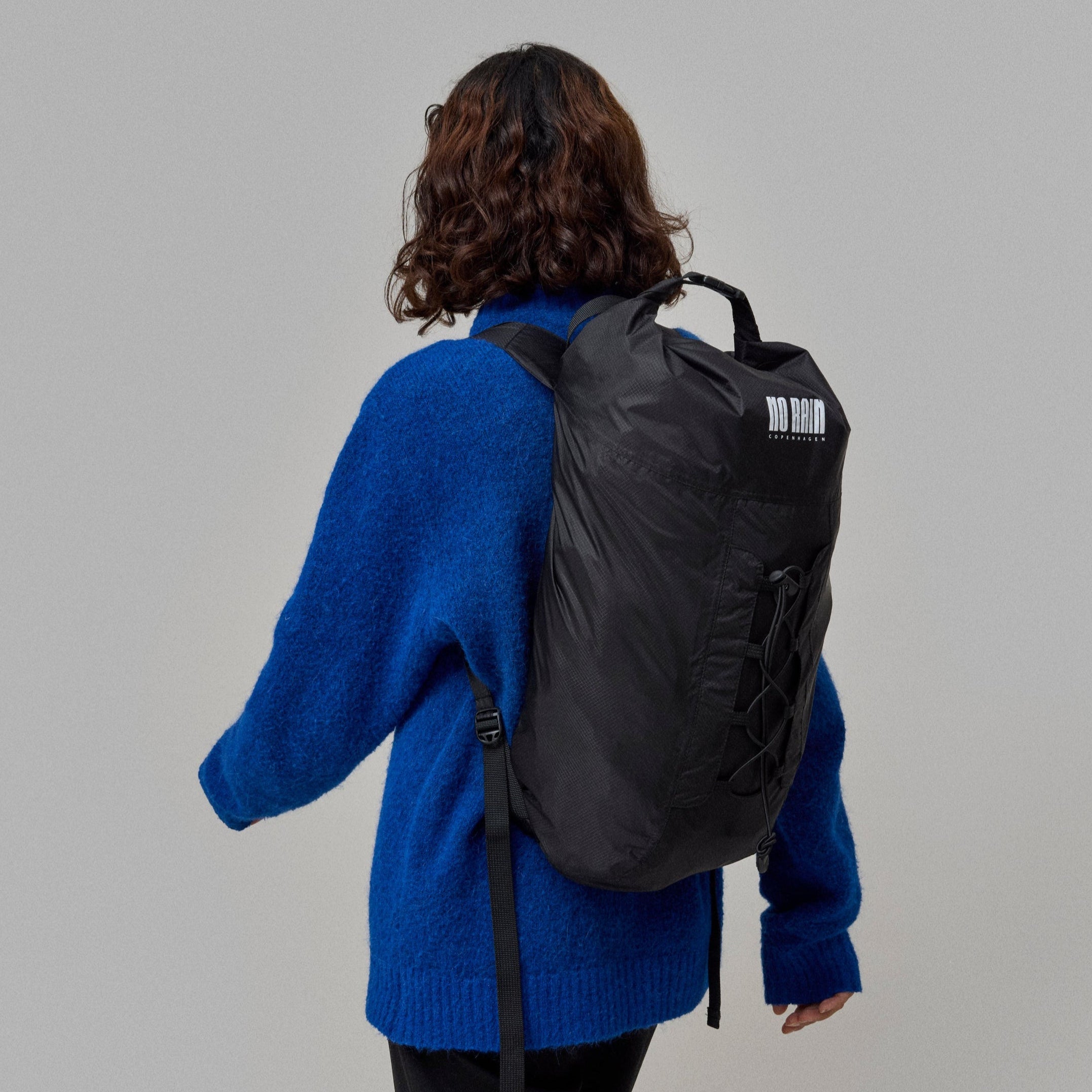 Person wearing a blue sweater and black Waterproof NoRain backpack on a plain background