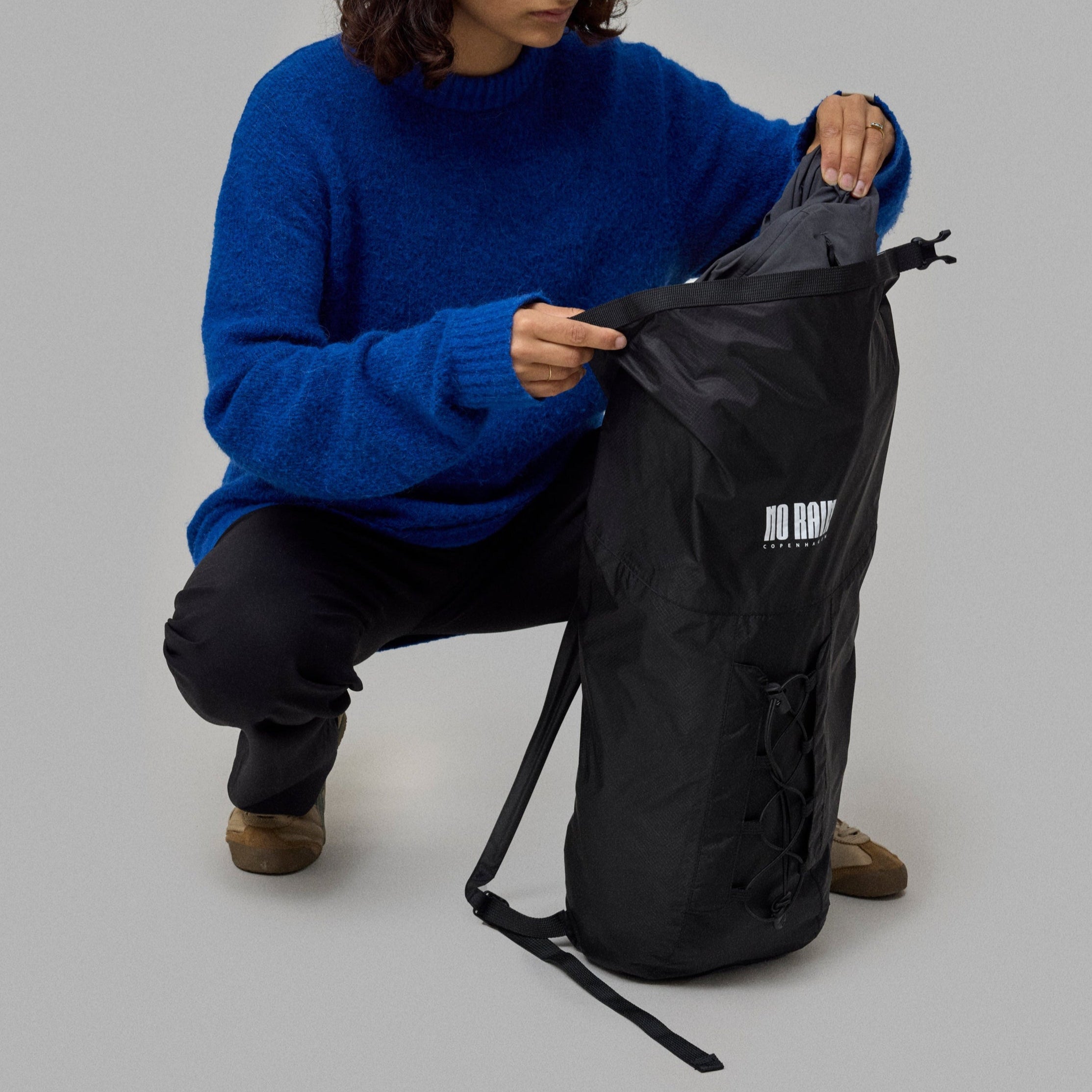 Person in a blue sweater opening a black bag on a gray background